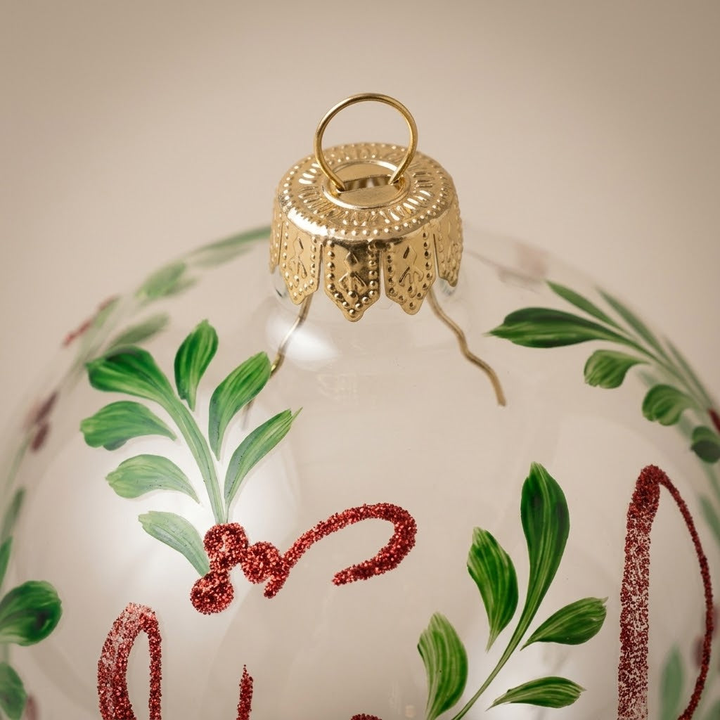 Dettaglio del decoro dipinto a pennello: scritta Noël in glitter rosso con foglie verdi su vetro trasparente